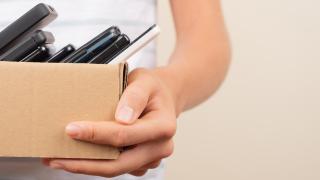     Anfrage erfolgreich  Hier ist ein passender Alt-Text für das Bild:  Nahaufnahme einer Person, die einen kleinen Pappkarton hält, der mit mehreren alten Mobiltelefonen und Smartphones gefüllt ist.
