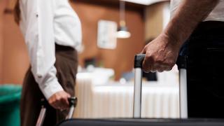 Zwei Gäste mit Rollkoffern gehen auf eine Hotelrezeption zu 
