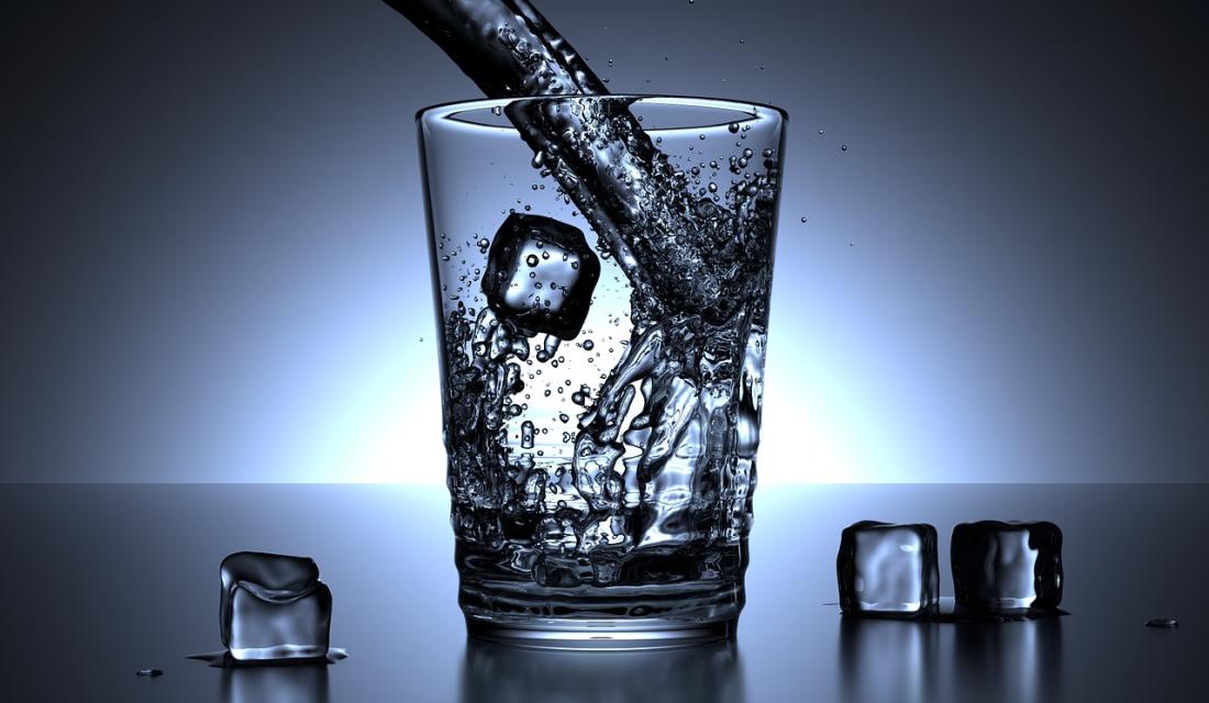 Wasser wird in ein Glas mit Eiswürfeln eingeschenkt