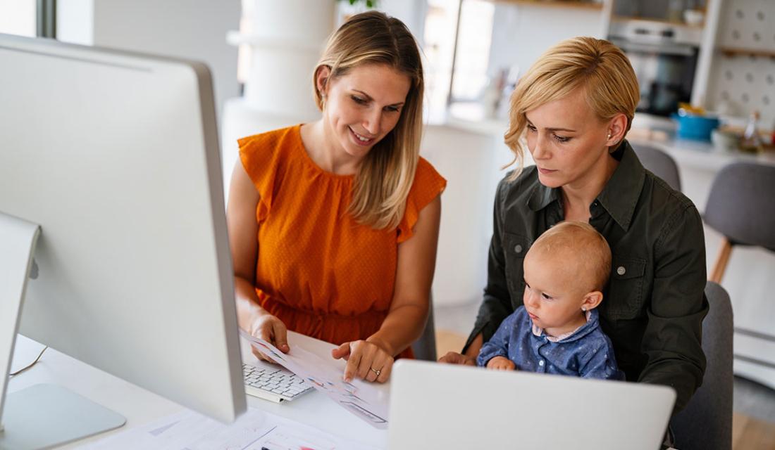 Eine Frau mit kleinem Kind sitzt neben einer Beraterin am Schreibtisch
